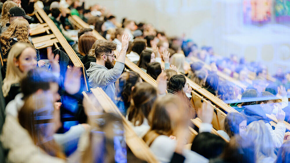 Ein voller Hörsaal mit Studierenden, die aufzeigen und interagieren.