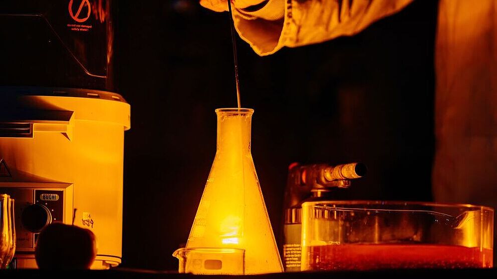 Orange leuchtendes Reagenzglas, in das ein brennender Stab gehalten wird