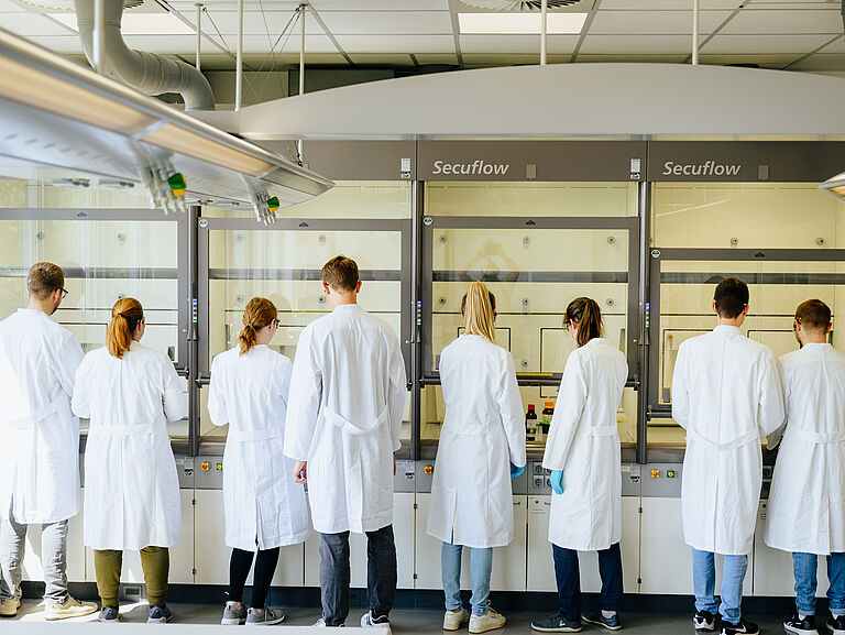 Eine Gruppe Chemie Studenten in Kitteln experimentieren an Abzügen
