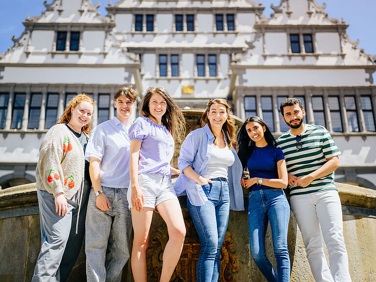 Sechs Studierende stehen vor dem Brunnen vorm Paderborner Rathaus und 